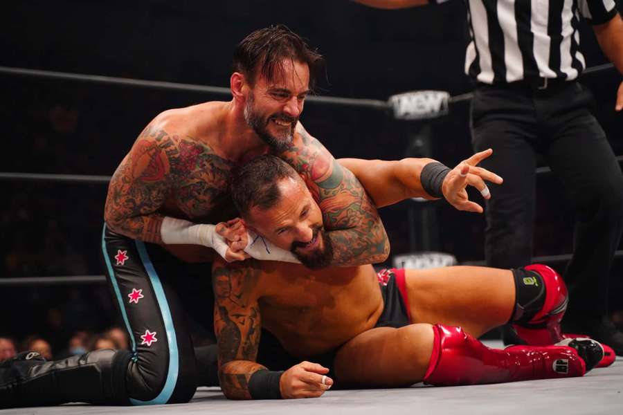 Dois lutadores travados em combate dentro de um ringue de luta com um árbitro por perto. — Combine Papéis de Parede