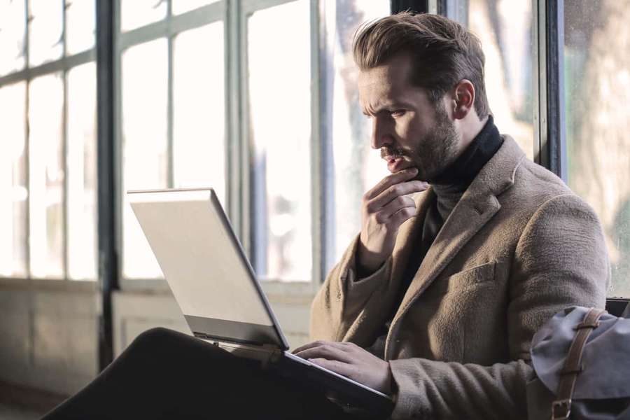 Man in coat using laptop by window in calm indoor setting — Competent Wallpaper
