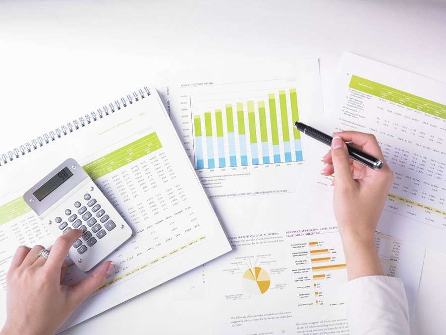 Pessoa calculando dados financeiros com gráficos e uma calculadora em uma mesa branca. — Contabilidade Papéis de Parede