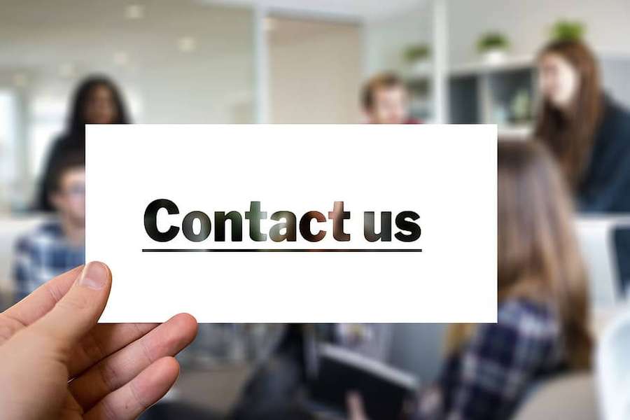 Mano sosteniendo una tarjeta de contacto en una oficina con colegas borrosos. — Contáctanos Fondos de pantalla