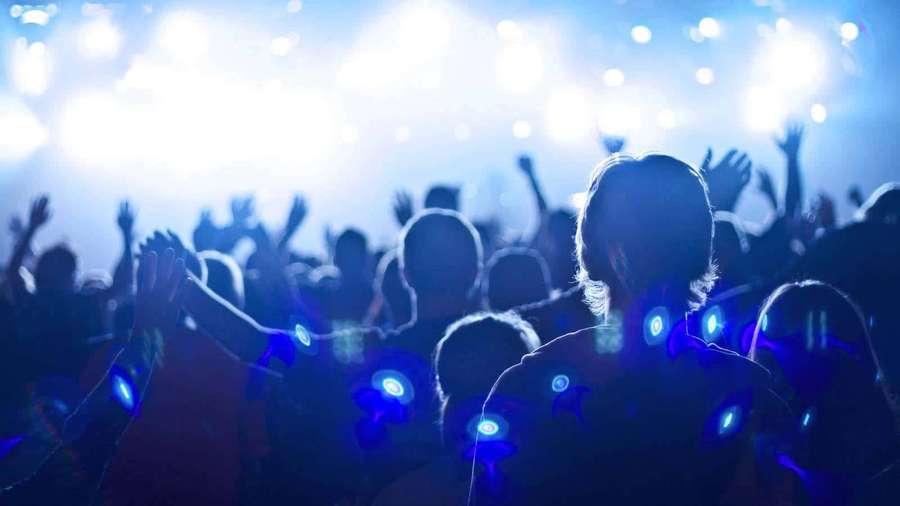 Multidão em um concerto com mãos levantadas e pulseiras brilhantes sob luz azul. — Contexto do concerto Papéis de Parede