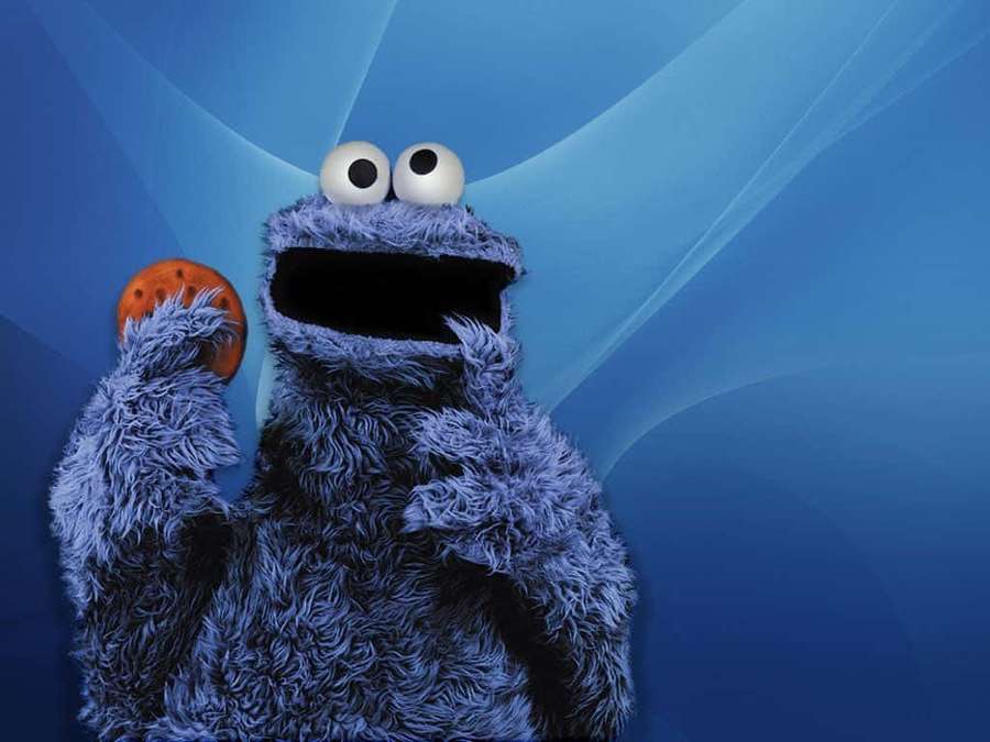Cookie Monster eagerly holds a chocolate chip cookie against a blue background. — Cookie Monster Background