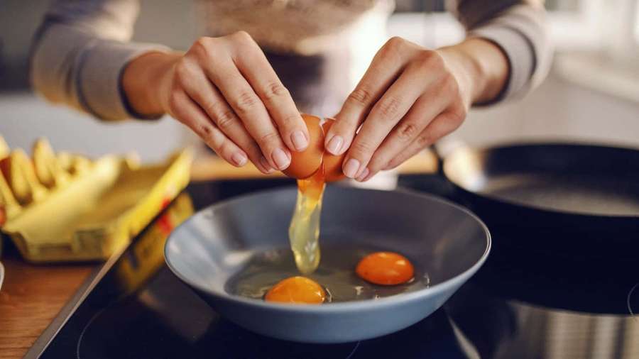 Person cracking an egg into a blue bowl on a kitchen counter. — Cooking Picture