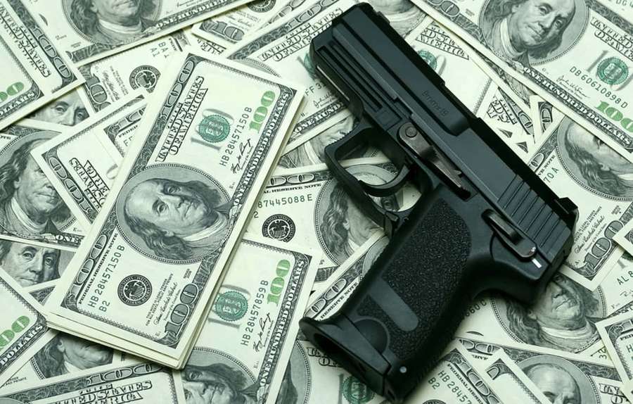 A black handgun lying on top of scattered one hundred dollar bills. — Cool Money Wallpaper