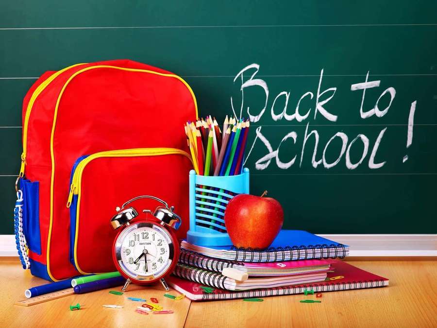 Red backpack and school supplies on wooden floor in front of green chalkboard with 'Back to School!' written in chalk. — Cool School Background