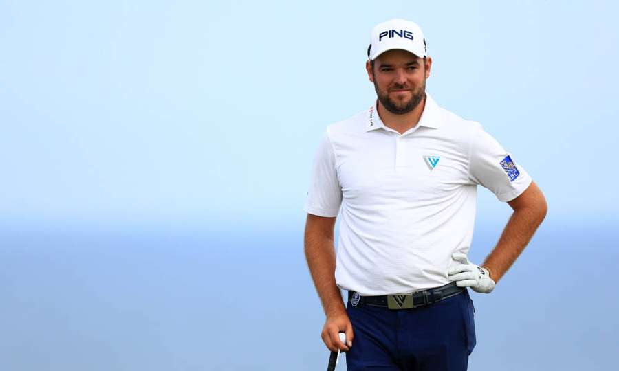 Professional golfer posing with club against blue sky background. — Corey Conners Wallpaper