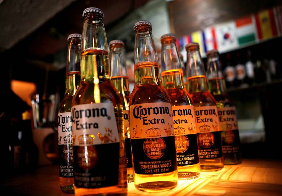 Fileiras de garrafas de cerveja Corona Extra em um bar de madeira com bandeiras ao fundo. — Coroa Papéis de Parede