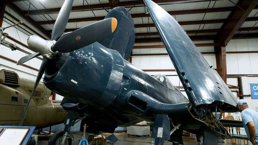 Vintage-Militärflugzeug im Hangar ausgestellt mit Techniker in der Nähe — Corsair Bilder