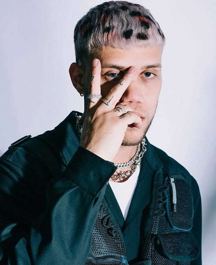 Man with leopard-print hair and tattoos posing in a dark jacket. — Cortez Background