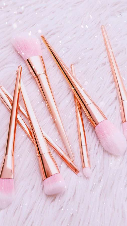 Brochas de maquillaje rosa dorado con cerdas rosas sobre una superficie blanca y esponjosa con purpurina. — Cosmético Fondos de pantalla