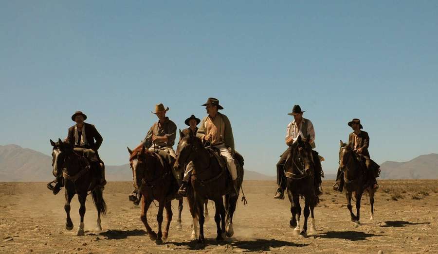 Five cowboys on horseback riding through a dry desert landscape. — Country Western Wallpaper