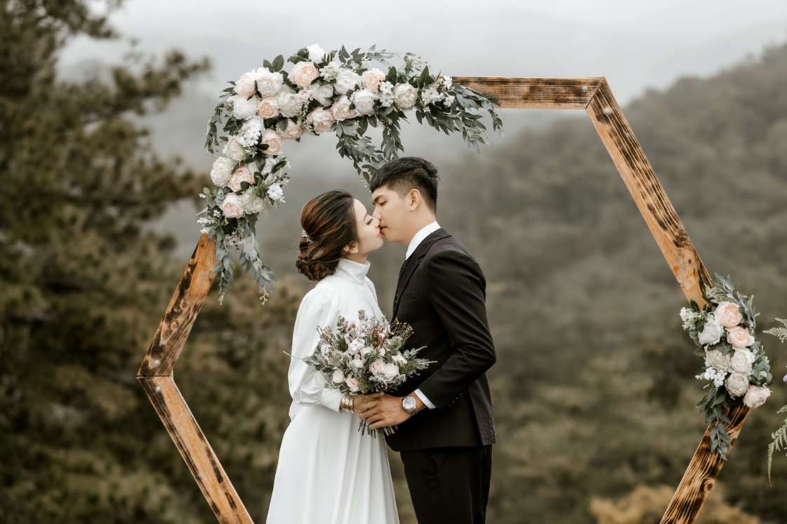 A bride and groom kiss under a wooden floral arch in a forest. — Couple Background