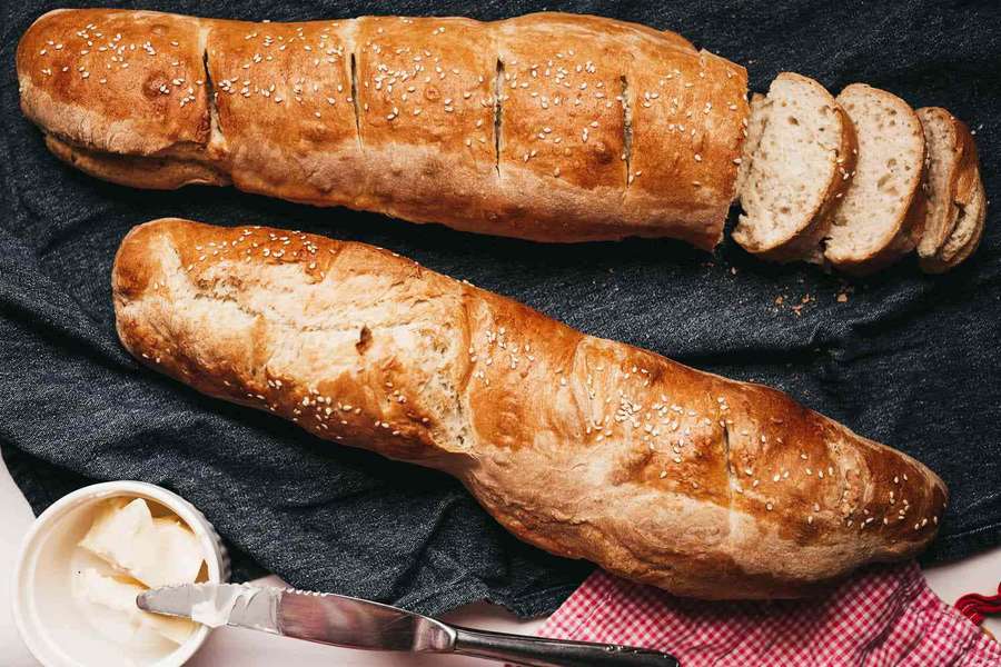 Two baguettes with sesame seeds and butter on a dark cloth with red checkered napkin. — Crusty Wallpaper