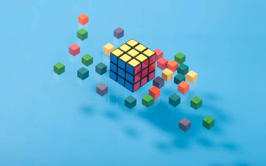A solved Rubik's cube with scattered colored cubes on a blue background. — Cumulative Wallpaper