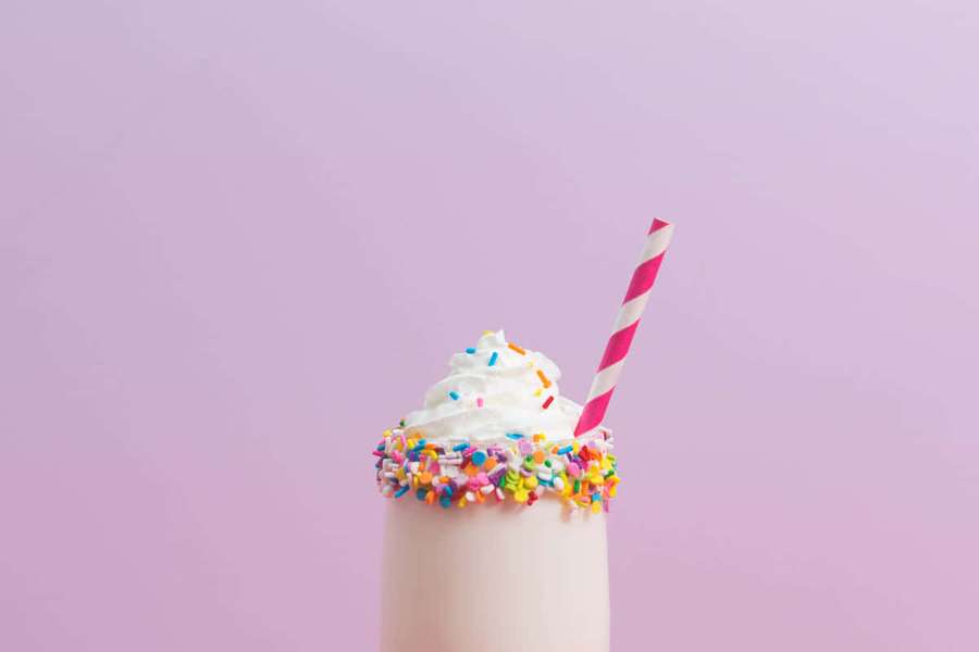 A milkshake with whipped cream and sprinkles on a pink background. — Cute Dessert Wallpaper