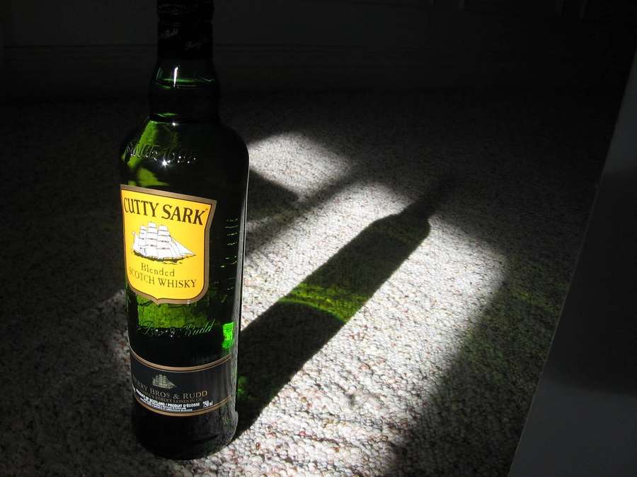 Green whisky bottle in bright sunlight on speckled counter casting long shadow. — Cutty Sark Wallpaper