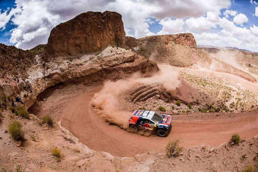 Rally car racing through dusty desert canyon with spectators watching — Dakar Wallpaper
