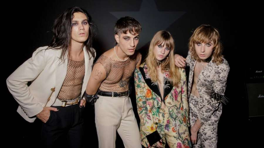 Four fashion models posing in avant-garde outfits against a dark background. — Damiano David Background