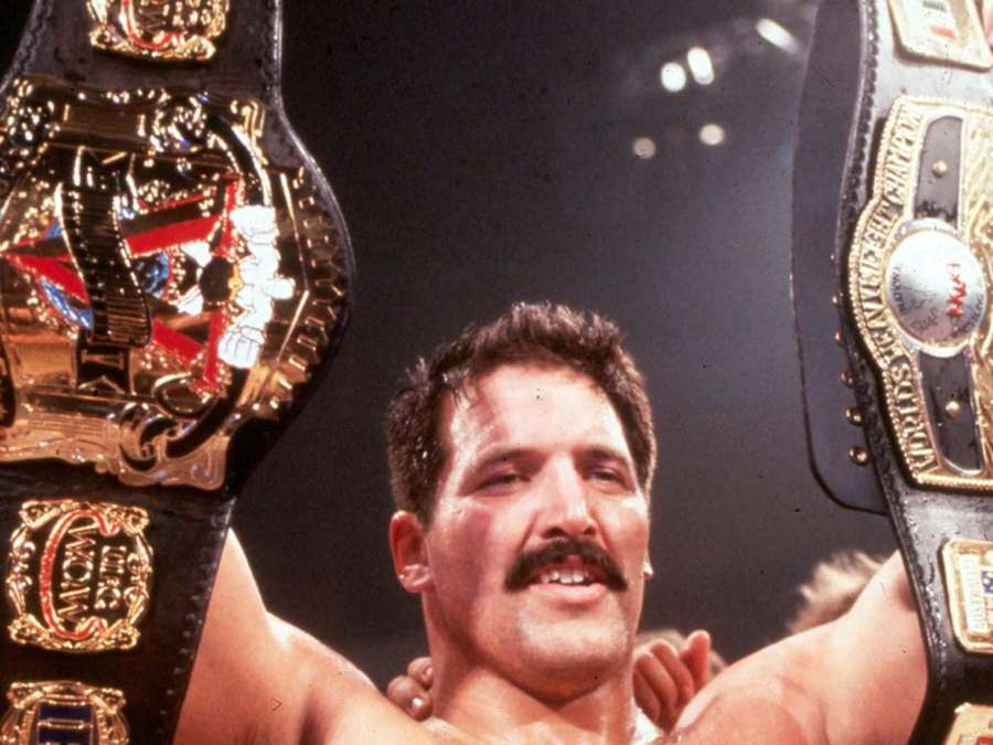 Wrestler holding two championship belts in victory pose under arena lights. — Dan Severn Wallpaper