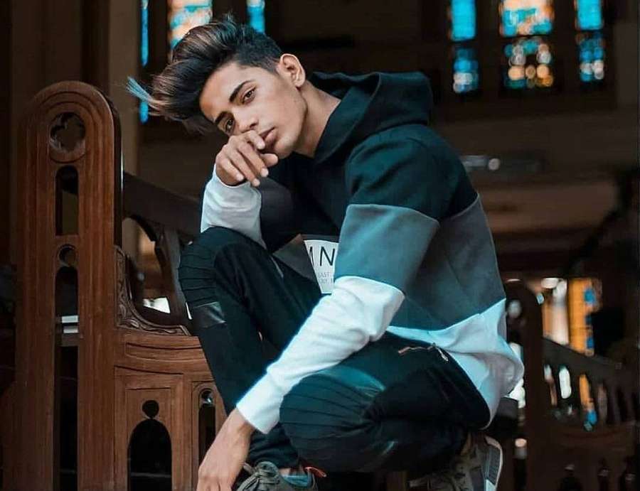 Joven con sudadera sentado en banco de iglesia con vidrieras detrás. — Danish Zehen Fondos de pantalla
