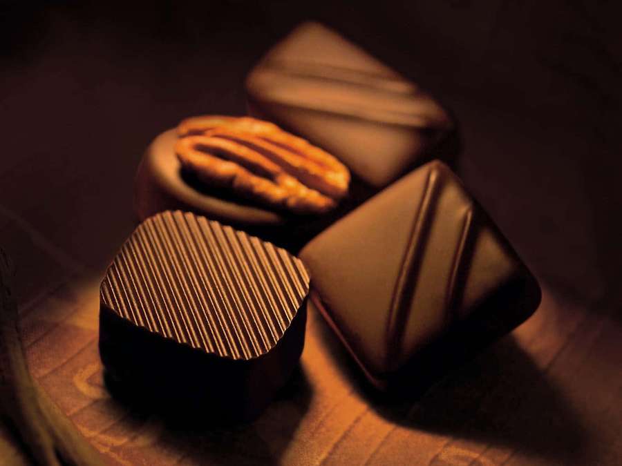 Luxurious dark chocolates with nuts and textured designs on wooden surface. — Dark Chocolate Wallpaper