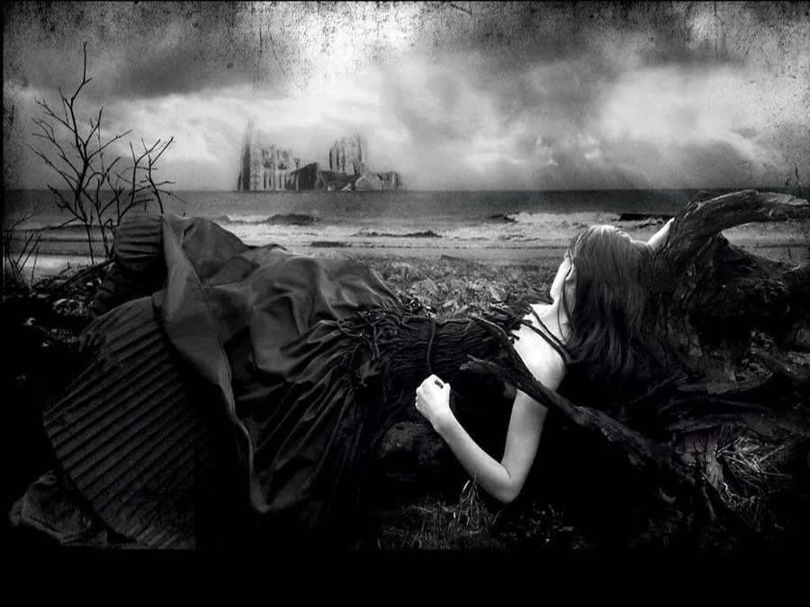 Nainen tummassa mekossa makaa rannalla katsoen raunioitunutta katedraalia myrskyssä. — Dark Gothic Taustakuvat