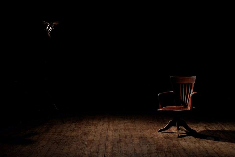 A wooden chair illuminated by a spotlight in a dark empty room. — Dark Room Wallpaper