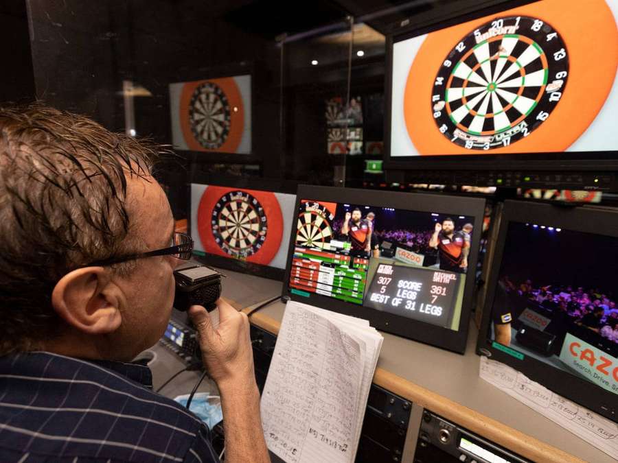 Kommentator im Studio sieht Dartspiel auf mehreren Bildschirmen. — Darts Bilder