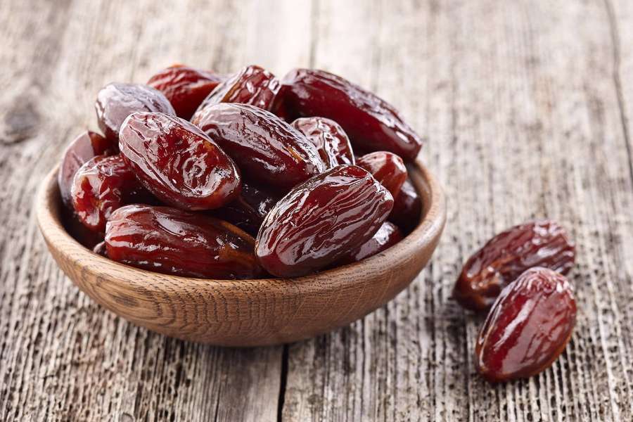 A wooden bowl filled with plump dark red dates on a weathered wood surface. — Dates Wallpaper