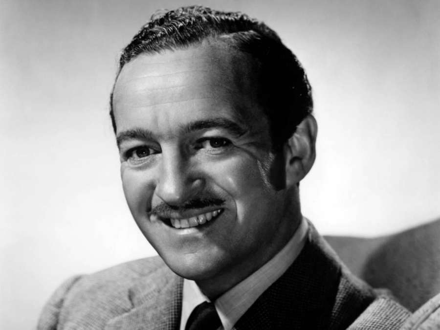 A smiling man with a mustache wearing a suit in a black and white studio portrait. — David Niven Wallpaper
