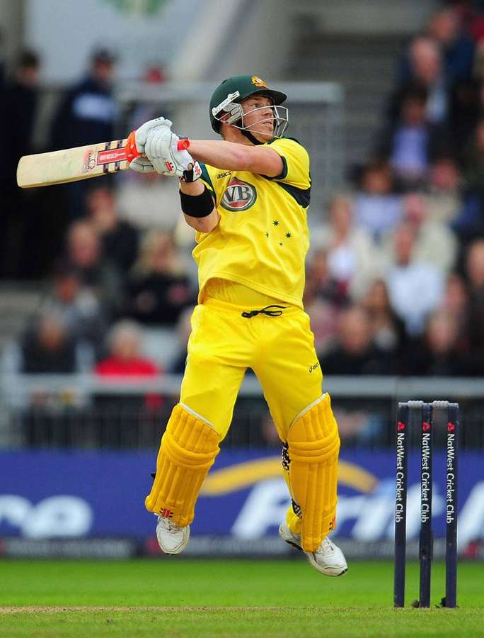 Cricketspieler in gelbem Trikot springt, um den Ball in der Nähe der Wickets zu treffen. — David Warner Bilder
