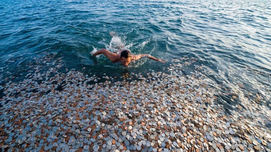 A top-down view of a person swimming in a sea of coins. — Debt Picture