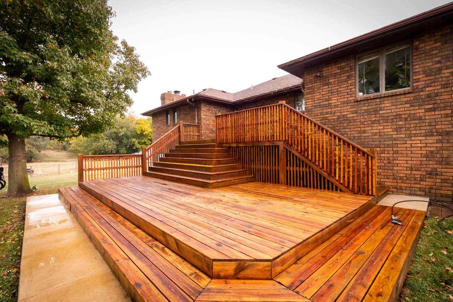 Wooden deck with stairs and railings attached to a brick house in a yard. — Deck Picture