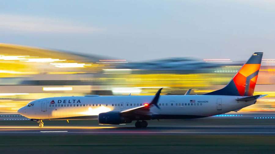 Delta-Flugzeug rast in der Dämmerung auf der Startbahn mit verschwommenen Terminallichtern. — Delta Wallpaper