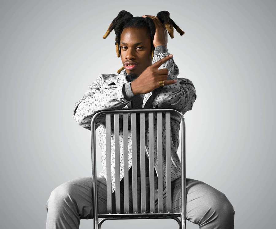 Mann mit Dreadlocks sitzt auf Metallstuhl und macht Handgeste im Studio — Denzel Curry Wallpaper