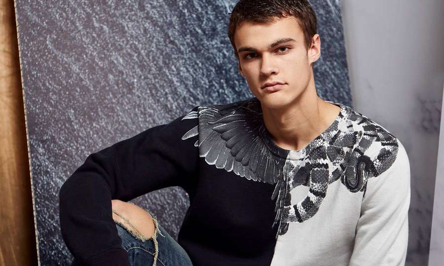 Junger Mann trägt einen schwarz-weißen grafischen Pullover mit Flügel- und Schlangenmotiven. — Designer-ästhetik Wallpaper