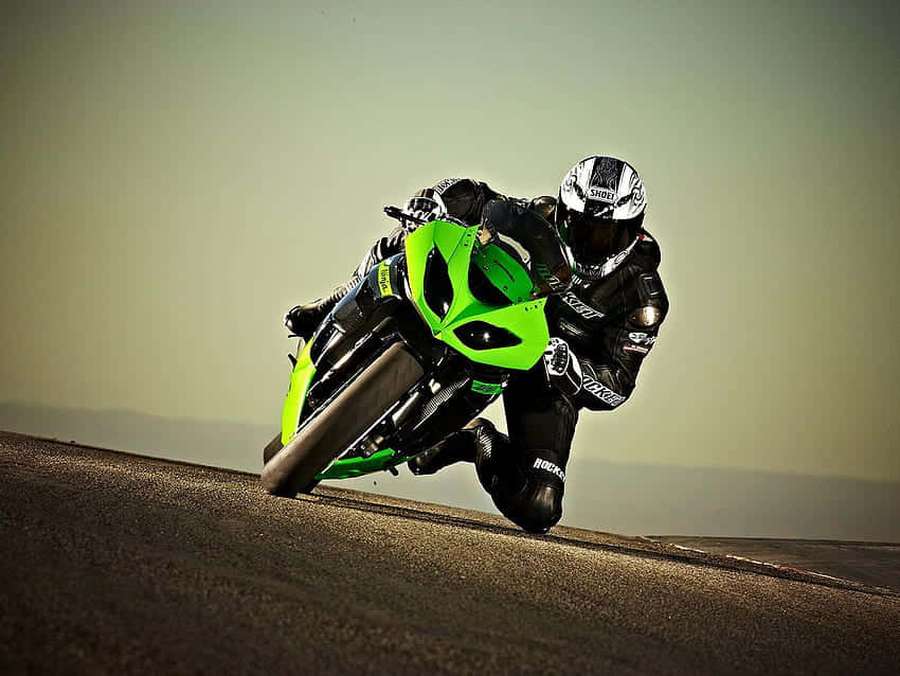 Motociclista com equipamento preto inclina-se em uma curva em uma Kawasaki verde em uma estrada pavimentada. — Desktop Kawasaki Papéis de Parede