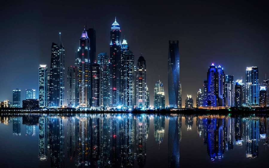 Horizonte noturno de arranha-céus iluminados refletidos em águas calmas. — Desktop profissional Papéis de Parede