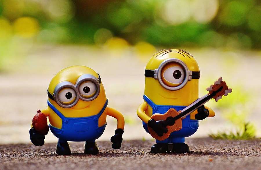 Two Minion toys one playing guitar the other holding an apple outdoors. — Despicable Wallpaper