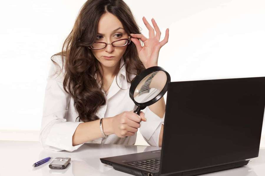 Woman using magnifying glass to examine laptop screen at desk — Detective Background
