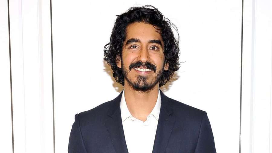 Man in donker pak glimlacht naar camera tegen witte achtergrond — Dev patel Achtergronden