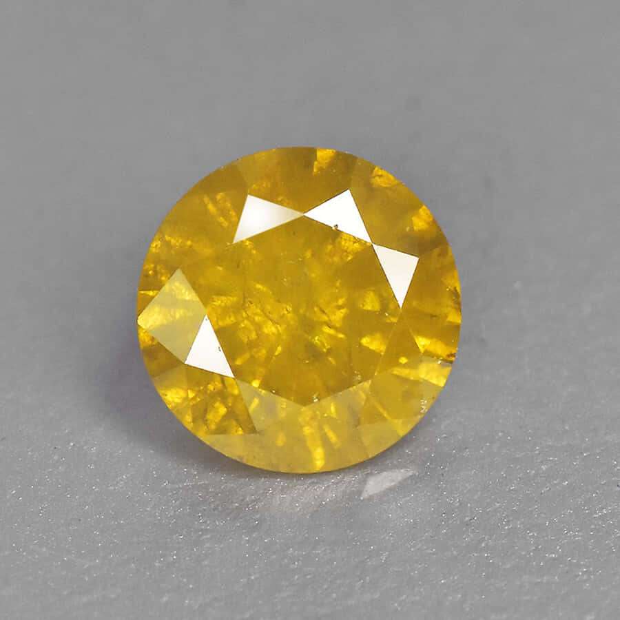 Una gema amarilla facetada descansando sobre una superficie gris. — Diamante Amarillo Fondos de pantalla