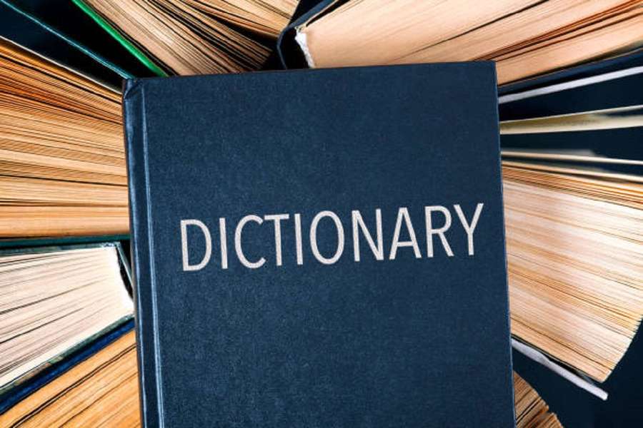 A dictionary book surrounded by stacks of other books. — Dictionary Wallpaper