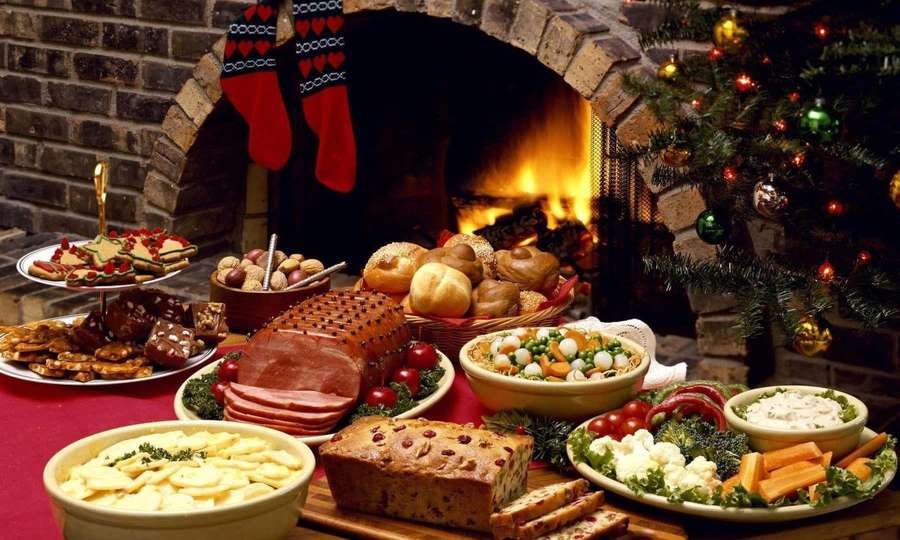 Christmas dinner spread with ham breads and snacks near a lit fireplace and decorated tree. — Dinner Picture