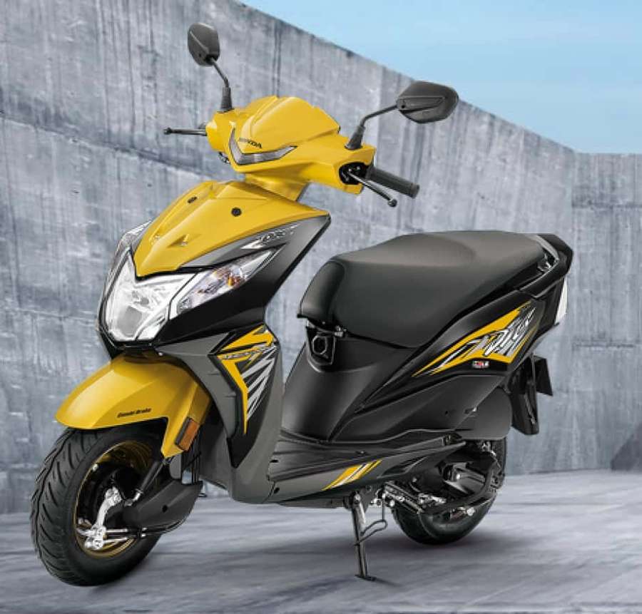 Yellow and black scooter parked against gray concrete wall. — Dio Bike Wallpaper