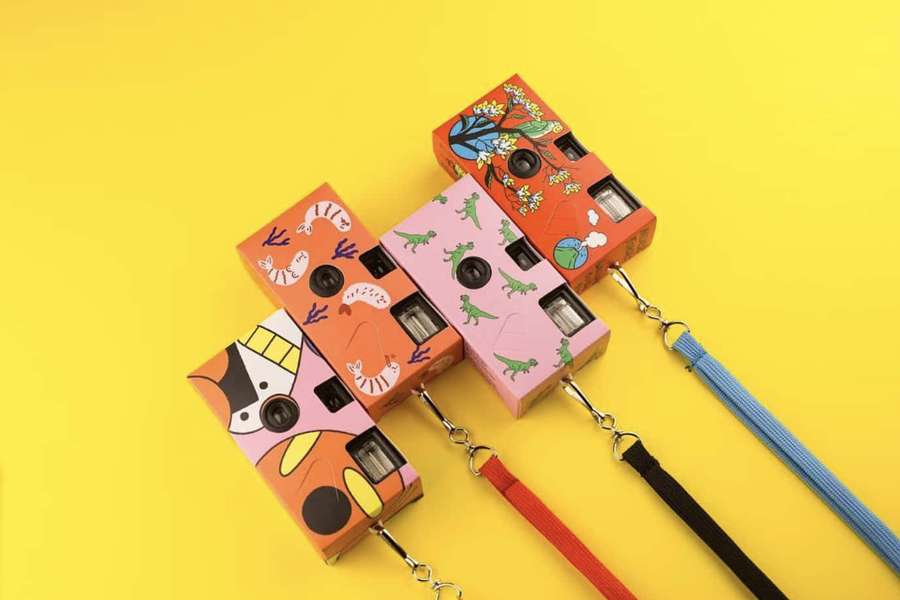 Four decorated toy cameras with straps on a yellow background. — Disposable Camera Picture