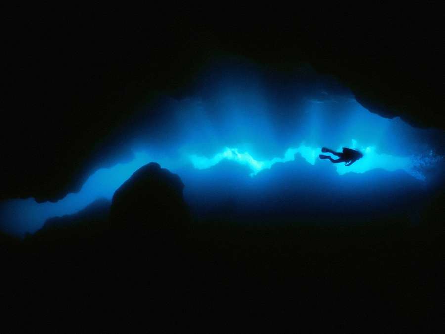 Diver exploring a glowing blue underwater cave entrance at night. — Diving Background