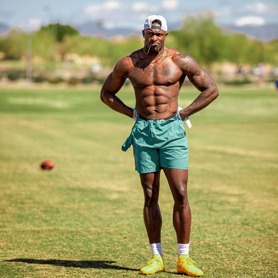 Athletischer Mann mit Tätowierungen auf einer Wiese, trägt tealfarbene Shorts und gelbe Schuhe. — Dk Metcalf Bilder