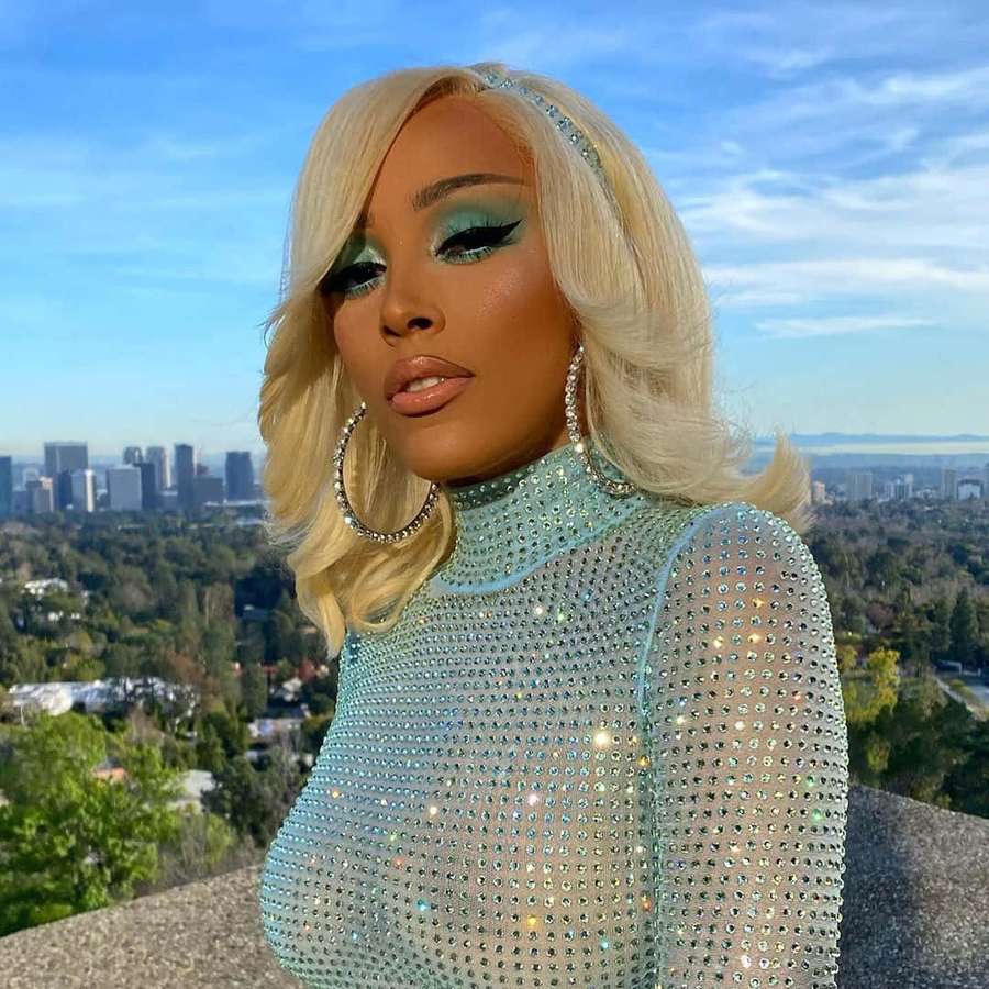 Frau in funkelndem blauen Outfit mit blonden Haaren und türkisfarbenem Make-up, die auf eine Stadt blickt. — Doja Cat Bilder