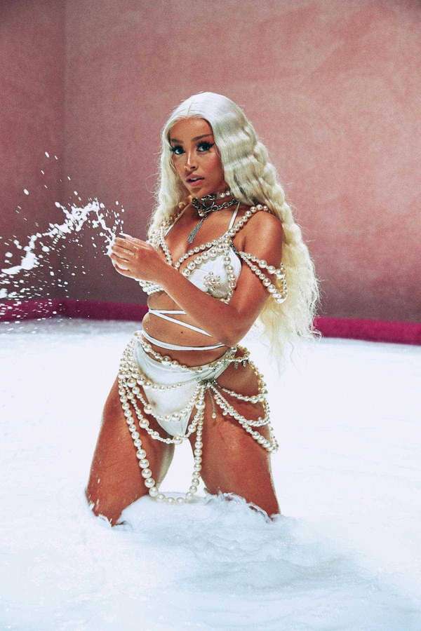 Woman in pearl outfit splashing water in foamy pool against pink wall. — Doja Wallpaper